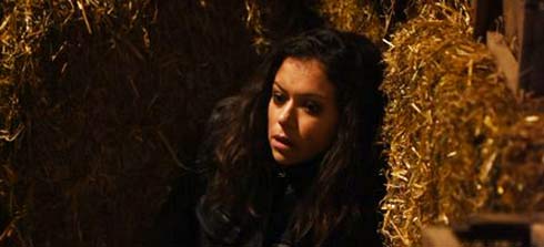 Tatiana Maslany as Sarah hides behind bales of hay