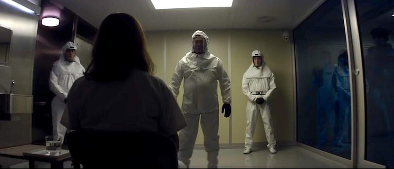 Lena in an isolation chamber with men in protective suits.
