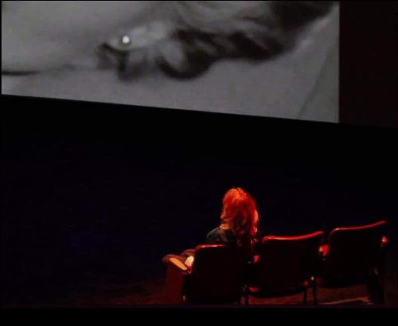 Nina Menkes in a theater seat watching the screen in Brainwashed: Sex-Camera-Power