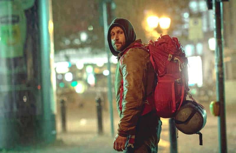 Max Riemelt in Sleeping Dog. He's dressed as a dirty homeless person in a blue hoodie wearing his daughter's red backpack.