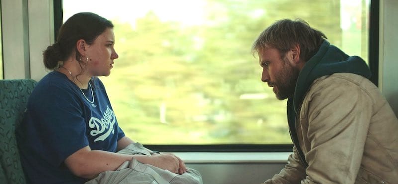 Max Riemelt and Tara Corrigan in Sleeping Dog. The are face to face on a train in serious conversation